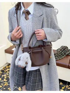 Detail of dark brown leather bucket bag with plush rabbit charm on grey wool coat