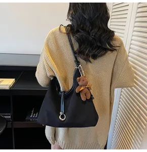 Detail of black suede hobo bag with metal buckle and cute brown bear pendant charm