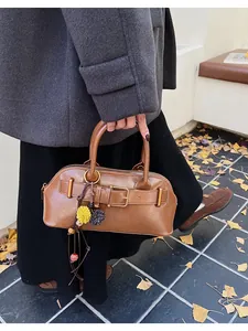 Close-up of brown leather shell bag with buckle strap and floral charm on autumn street