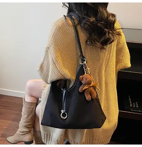 Detail of black suede hobo shoulder bag featuring a cute brown plush bear charm