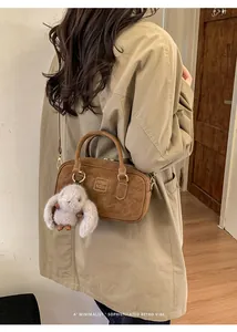 Detail of suede boston bag in brown with plush rabbit charm and embossed text