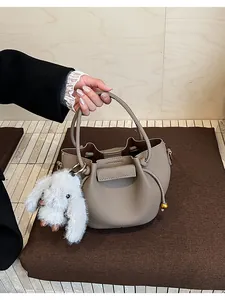 Detail of khaki pebbled leather bucket bag with drawstring and white plush rabbit charm