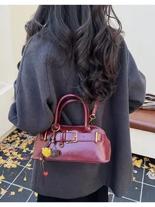 Detail of vintage burgundy shell bag featuring golden buckle and plush ball charm