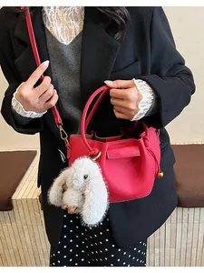 Red lychee grain leather bucket bag with white plush bunny charm and gold metal orb