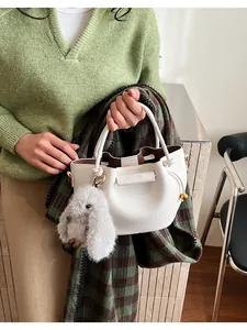 Detail of white lychee leather bucket bag with a gray plush rabbit charm accessory