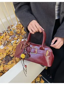 Detail of burgundy leather handbag with metal buckle and decorative pompom charm