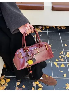 Close-up of burgundy shell bag with leather belt buckle and floral pompom charm