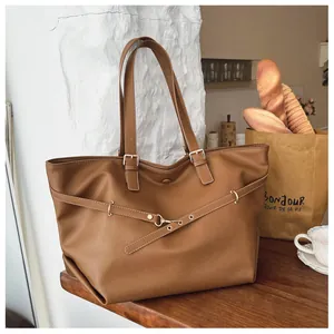 Dettaglio della borsa tote in pelle marrone con cinturini incrociati e fibbia dorata