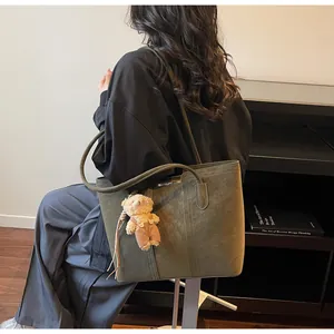 Dettaglio della borsa tote in pelle verde scuro con manici e ciondolo a forma di orsetto