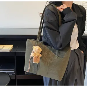 Dettaglio della borsa tote in pelle scamosciata oliva con cuciture e ciondolo a orsetto