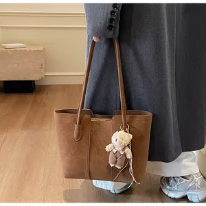 Borsa tote in camoscio marrone con ciondolo a orsetto indossata da una modella