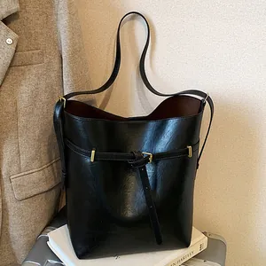 Minimalist black leather bucket bag with gold hardware on a stylish travel background