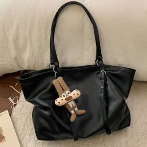 Minimalist black leather tote bag with a cute brown rabbit pendant on a cozy blanket