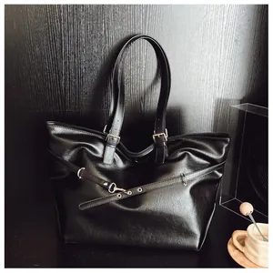 Dettaglio di una borsa tote nera minimalista con fibbia in metallo su fondo in legno scuro