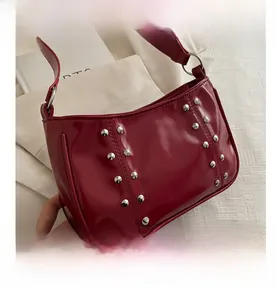 Detailed macro view of dark red patent leather shoulder bag with silver rivet accents
