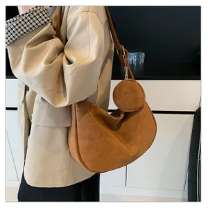 Detail of a brown suede half-moon crossbody bag with a small detachable round pouch