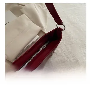 Detail of silver smooth metal zipper and rivet accents on red glossy underarm bag