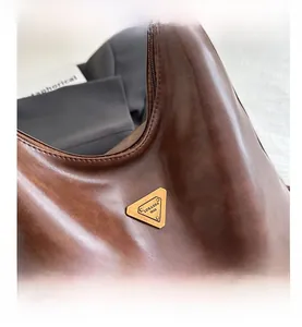 Close-up of vintage brown leather tote bag with metallic triangle logo and zipper detail