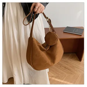 Detail of a brown suede crescent bag with a gold metal logo and a round coin purse charm