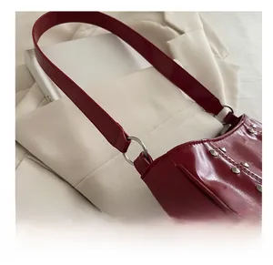 Close-up of wine red leather crossbody bag with silver rivet details and wide strap