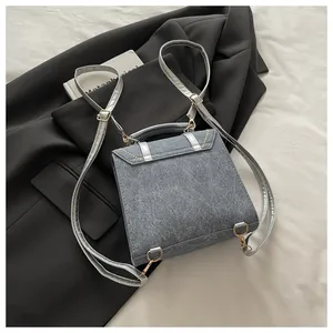 Détail d'un sac à dos en denim gris avec bretelles métalliques et bords à rivets