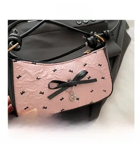 Detailed view of pink textured fabric with black bow and metal heart charm on shoulder bag