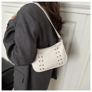 Detail view of a white shoulder bag with silver rivets worn by a model in a grey blazer