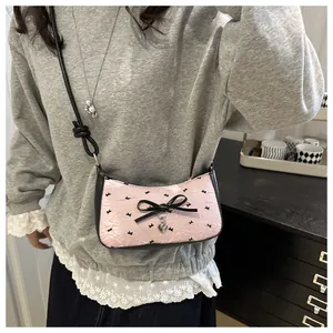 Close-up of pink textured shoulder bag featuring black bow detail and heart pendant charm