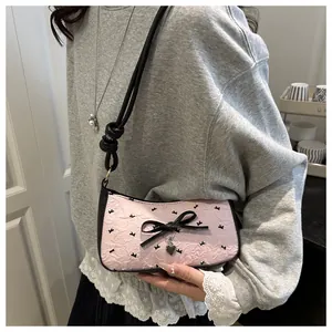 Detail of pink pleated underarm bag with black bow and heart charm on a grey sweater