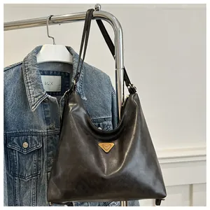 Detail shot of black leather tote bag with a golden triangle emblem on a denim jacket