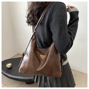 Detail of a dark brown soft leather tote bag with a golden triangle logo and adjustable strap