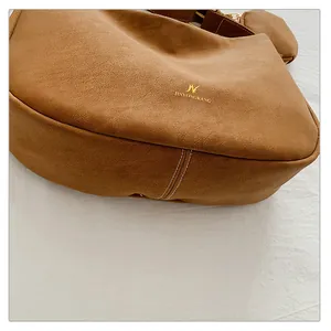 Close-up of brown suede crossbody bag with gold brand logo and white contrast stitching