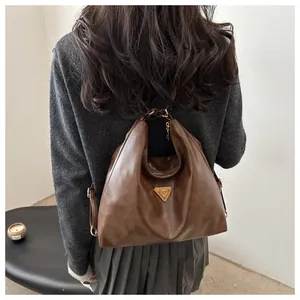Detail showing brown vintage tote bag in use with triangular metal logo and slim strap