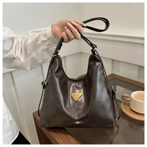 Detail of a dark brown glossy leather tote bag with a golden triangular metal plaque