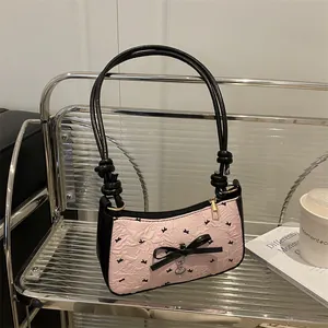 Pink bird print shoulder bag with black bow and silver heart pendant on metal shelf
