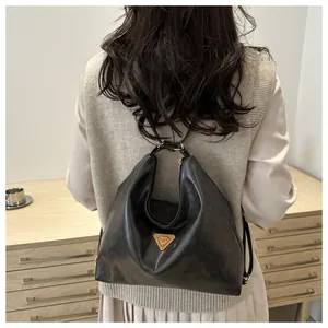 Detail of minimalist black leather tote bag featuring triangular metal emblem on soft texture