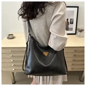Detail view of a large black faux leather tote bag with a golden triangular logo