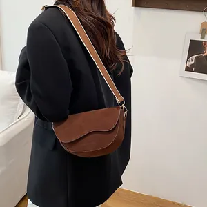 Braune Wildleder-Satteltasche mit breitem Canvas-Gurt am Modell in gemütlichem Raum