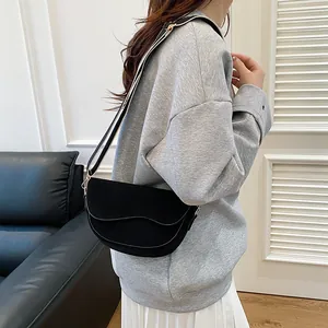 Schwarze Satteltasche mit breitem Streifenriemen am Model in modernem Interieur gezeigt