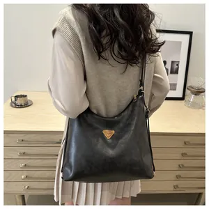 Detail of a large black soft leather tote bag with a metallic triangular plaque on front