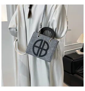 Modella indossa borsa tote in feltro grigio con lettere AB nere e dettagli dorati