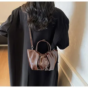 Détail d'un sac nuage en cuir verni marron foncé plissé porté en bandoulière par un mannequin