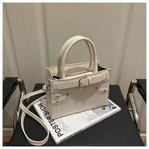 Detail view of cream white shoulder bag with decorative buckle straps and metal rivets
