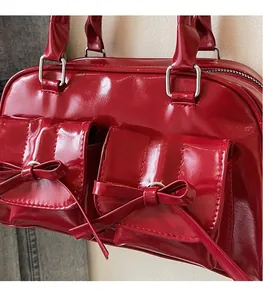 Detail of red patent leather handbag featuring glossy texture and twin bow decorations