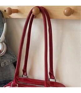 Detail of red patent leather shoulder bag with sleek straps on a wooden hook