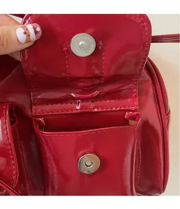 Detailed macro view of silver magnetic hardware buckle on red glossy patent leather handbag