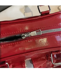 Close-up of a silver metal zipper on a red glossy leather shoulder bag detail