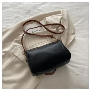 Close-up of black cylinder crossbody bag with brown strap and golden hardware
