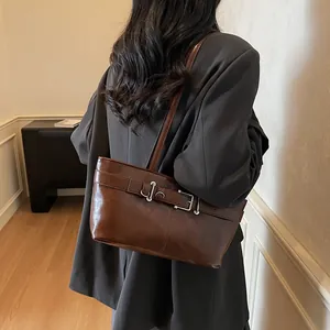 Sac bandoulière vintage marron avec boucle, porté par un mannequin dans un cadre épuré