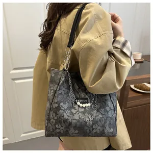 Detalle de bolso tote gris con estampado floral, cadena plateada y adorno de perla